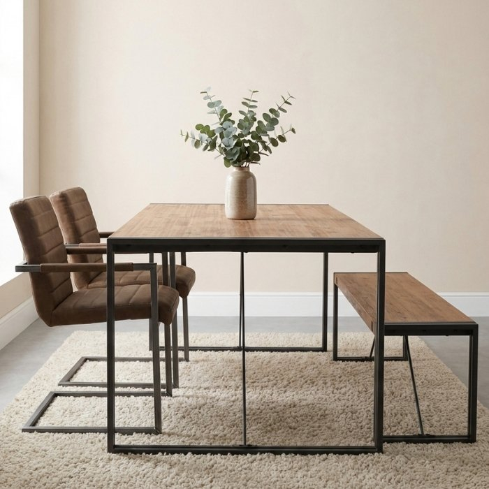 Industriële eettafel met houten blad en zwart metalen onderstel, gedekt met een vaas eucalyptus en omringd door vier bruine lederlook stoelen op een tapijt