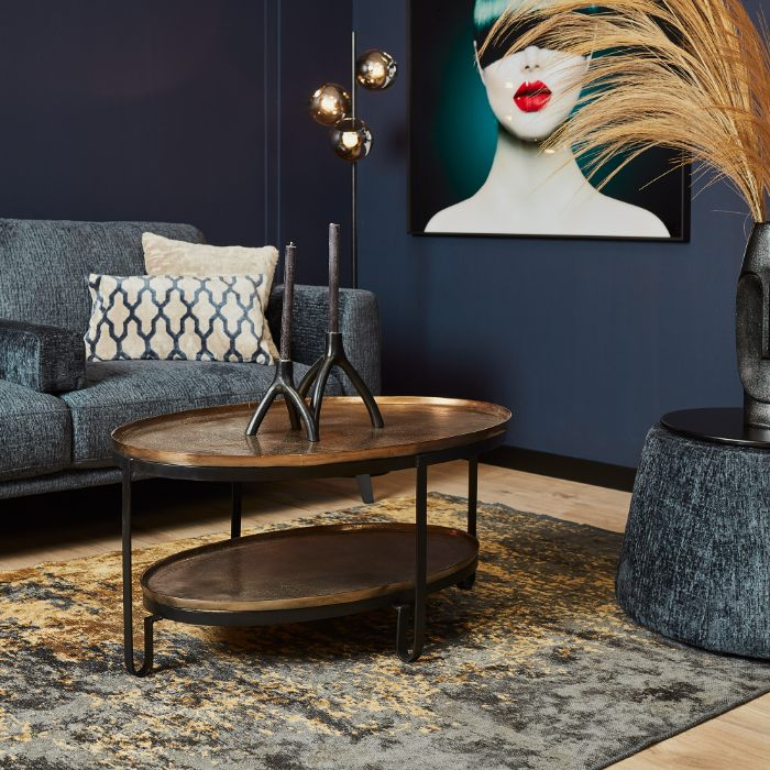Ovale salontafel Kate met goudkleurig blad en zwart metalen frame bij een blauwe bank