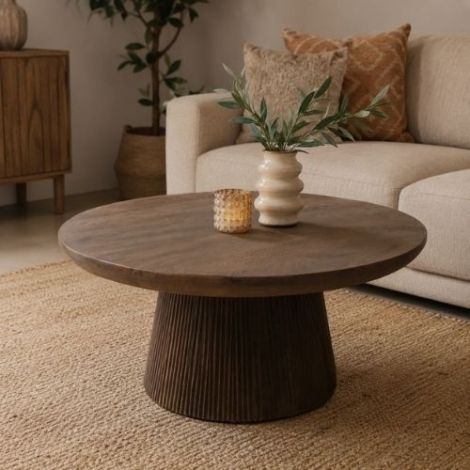 Ronde bruine bijzettafel van 80 cm met geribbelde voet in een woonkamer naast een bank, met vaas en kussens